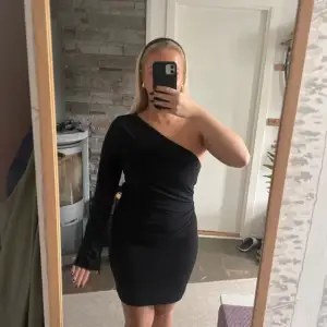 Säljer en elegant svart oneshoulder klänning från H&M. Perfekt för festliga tillfällen! Klänningen är tight och har en lång ärm på ena sidan, vilket ger en stilren look. Materialet är mjukt och bekvämt, vilket gör den skön att bära hela kvällen. Passar perfekt för höst och vinter.