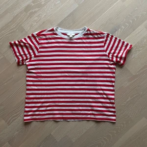 Röd och vit randig t-shirt från H&M - Säljer en klassisk röd och vit randig t-shirt från H&M. Den har en rund halsringning och korta ärmar, perfekt för en avslappnad stil. T-shirten är tillverkad i mjuk bomull för extra komfort. Perfekt till sommaren! 🌹