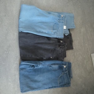 Tre par jeans i olika färger - Säljer tre par jeans i olika färger: ljusblå, svart och mörkblå. Alla byxorna har en klassisk femficksdesign och knappgylf. Perfekta för en avslappnad stil.