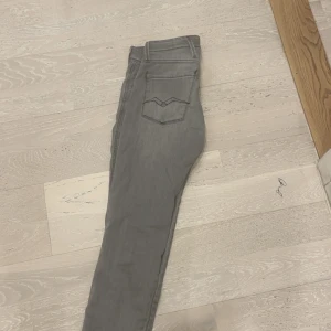 Grå Replay slim anbass jeans - Snygga grå jeans från Replay i slim fit anbass med klassiska fem fickor och diskreta sömmar på bakfickorna. Jeansen har normal midja och är tillverkade i mjukt jeanstyg med lite stretch för extra komfort. Perfekta för en clean och stilren look. Liten fläck finns på undersidan av fickan. Priset kan absolut diskuteras.