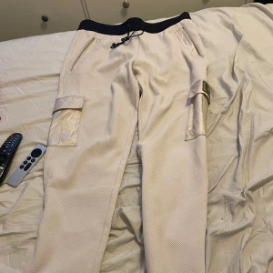 Beige mjukisbyxor från Emporio Armani - Snygga beige mjukisbyxor från Emporio Armani med praktiska cargofickor och justerbar midja med snörning. Storlek L men funkar som M, jag är 178 och dom sitter lite baggy. Perfekta för en avslappnad stil med en touch av lyx. EA7-logga på benet ger en exklusiv känsla. Dessa är använda 1 gång så vill bli av med dom, köpte dom för 2000 nypris, de har inga defekter och är väldigt sköna att både ha ute och när man tar de lugnt hemma, pris kan diskuteras vid snabb affär , hör av er vid funderingar!