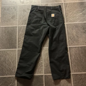 Svarta byxor från Carhartt - Säljer ett par svarta byxor från Carhartt med en klassisk design. Dom är knappt använd och är i storlek 30/32