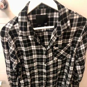 Svartvit rutig skjorta från 157 - Snygg svartvit rutig skjorta från 157 med klassisk krage och knappar framtill. Perfekt för en avslappnad stil. Skjortan har långa ärmar och en bröstficka för extra stilpoäng.