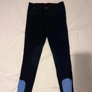 Svarta ridbyxor med stjärndetaljer - Snygga svarta ridbyxor med ljusblå detaljer och broderade stjärnor på baksidan. Byxorna har en knapp framtill och är designade för en bekväm passform under ridning.