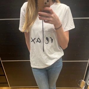 Vit t-shirt med tryck - Säljer en vit t-shirt med ett stilrent tryck i svart. T-shirten har en normal passform och korta ärmar, perfekt för en avslappnad look. Passar bra till jeans eller shorts.