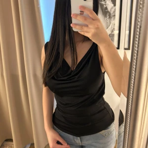 Svart ärmlös topp från BikBok - Snygg svart ärmlös topp från BikBok i en elegant draperad stil. Perfekt för en stilren look, med en mjuk och följsam passform. Toppen har en v-ringad design som ger en chic touch. 😍