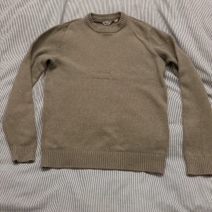 stickad tröja från Dobber  - Säljer en stilren beige stickad tröja från Dobber. Tröjan har långa ärmar och ribbade muddar vid ärmslut och nederkant. Perfekt för kyligare dagar och enkel att matcha med olika outfits.