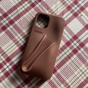 Brunt mobilskal från rhode - Snyggt rosa mobilskal från Rhode med en unik design som inkluderar ett grepp på baksidan. Perfekt för att skydda din telefon och ge den en personlig touch. Skalet har en öppning för kameran och är lätt att sätta på och ta av. Köpt utomlands i en marknad i Spanien för 350 kr! För iPhone 12 och är aldrig använd 🥰