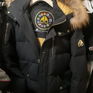 Svart dunjacka från Moose Knuckles - Moose Knuckles vinterjacka med päls huva och guldfärgade dragkedjor, storlek S. Jackan har inga större defekter, en fläck på innersidan av jackan men ingenting som syns när man har på sig (bild 5). Säljer åt min pappa, pris kan diskuteras vid snabb affär