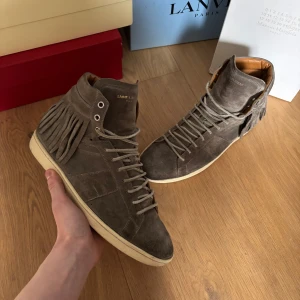 Grå mocka sneakers från Saint Laurent - Snygga grå sneakers i mocka från Saint Laurent med fransdetaljer på sidan. Skorna har snörning och en bekväm innersula i skinn. Perfekta för en stilren look. Vid intresse hör av dig för mer information✌️