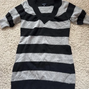 Randig tröja från GANT - Säljer en snygg randig tröja från GANT i svart och grått. Tröjan är tillverkad av 70% lammull vilket gör den både varm och bekväm. Den har en v-ringad hals och trekvartsärmar, perfekt för kyligare dagar. liten i storlek, mer som en medium.