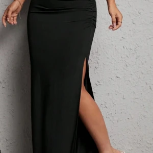 Svart kjol med slits - Elegant svart kjol med en stilren slits på sidan. Perfekt för en kväll ute eller en speciell tillställning. Kjolen har en smickrande passform som framhäver figuren. Nyskick!