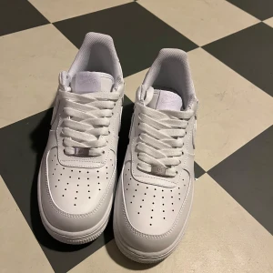 Vita Nike Air Force sneakers - Säljer ett par klassiska vita Nike Air Force sneakers. Skorna har en stilren design med perforerade detaljer på tån och snörning framtill. Perfekta för en casual look.  Saknas skobox pris, pris kan diskuteras!