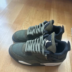 Nike Air Jordans i olivgrön färg - Säljer ett par olivgröna Nike Air Jordans med svart och vit detaljering. Skorna har en klassisk snörning och är tillverkade i mocka. Perfekta för sneakerheads som vill ha en unik stil. Använda ett par gånger men för små för mig. Kostar 3000kr på stockx
