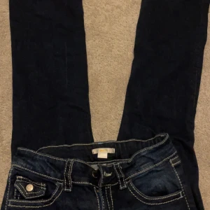 Mörkblå jeans med kontrastsömmar - Snygga mörkblå jeans med vita kontrastsömmar och klassisk femficksdesign. De har en knapp och dragkedja framtill samt dekorativa sömmar på bakfickorna. Perfekta för en avslappnad stil. Andvänd få tal gånger o ser helt oanvända ut.❤️