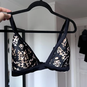 Leopardmönstrad bikiniöverdel - Snygg bikiniöverdel med leopardmönster och svarta detaljer. Den har breda axelband och en enkel knäppning bak. Perfekt för en trendig look vid poolen eller stranden. Använd ett par gånger max.