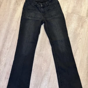 Svarta jeans med fickdetaljer - Snygga svarta jeans med framträdande fickor fram och bak. Byxorna har en bootcut-stil och är lågmidjade för en bekväm passform. Perfekta för en stilren look.