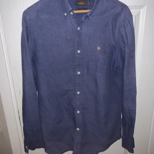 Blå skjorta från Morris - Snygg blå skjorta från Morris med broderad detalj på bröstet. Skjortan har långa ärmar och knappar framtill. Perfekt för en stilren look.