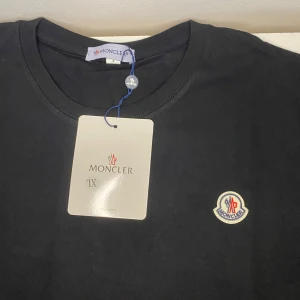 Svart t-shirt från Moncler - Snygg svart t-shirt från Moncler med deras ikoniska logga broderad på bröstet. T-shirten har en klassisk rund hals och är kortärmad, perfekt för en stilren look.  Den passar mer som S-M men den ör riktigt bra kvalitet .  Om du skickar ett seriöst bud så kommer jag acceptera 