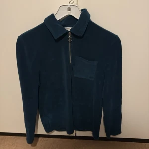 Mörkblå fleecejacka med dragkedja - Säljer en stilren mörkblå fleecejacka med dragkedja och en praktisk bröstficka. Jackan har en klassisk krage och långa ärmar, perfekt för kyliga dagar. Passar både till vardags och mer avslappnade tillfällen.