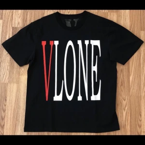 Vlone T-shirt - Svart t-shirt från Vlone med stort tryck av 'VLONE' i vitt och rött på framsidan och ett stort rött 'V' på baksidan. Säljer för har ingen användning av den mera, men den är perfekt för en avslappnad ”look” då modellen är baggy av sig själv.