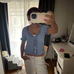 Blå kofta - Säljer en söt blå ribbad topp med knappar framtill och volangdetaljer. Koftan har korta ärmar och en v-ringad design. 