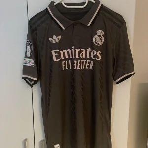 Real Madrid fotbollströja 24/25 - Snygg grå Real Madrid tröja med Camavinga och nummer 6 på ryggen. Heläkta och i nyskick. Spelarversion, alltså den spelarna har på sig samt den dyrare versionen. Storlek M. 