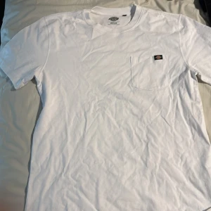 Vit t-shirt från Dickies - Säljer en klassisk vit t-shirt från Dickies i storlek medium. T-shirten har en bröstficka med Dickies-logga och är tillverkad i mjuk bomull. Perfekt för en avslappnad stil. Väldigt oversized