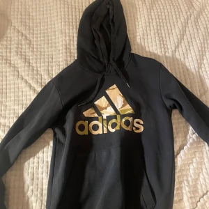 Adidas hoodie - Säljer en svart hoodie från Adidas med ett coolt camouflagemönster i loggan. Tröjan har en klassisk passform med huva och dragsko samt en stor magficka framtill. 