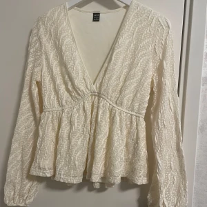 Vit omlottopp från Shein - Säljer en elegant vit omlottopp från Shein med långärmade ärmar och ett subtilt mönster. Toppen har en v-ringad design och är perfekt för en stilren look. Passar bra till både jeans och kjol. Perfekt för vår och sommar!