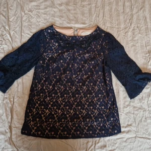 Mörkblå spetsblus från Oasis - Elegant mörkblå spetsblus från Oasis med trekvartsärmar och vackert blommönster. Blusen har en rund halsringning och en liten öppning bak. Perfekt för en stilfull look.