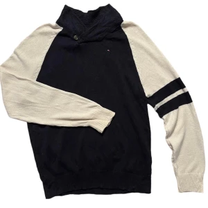 Mörkblå och vit tröja från Tommy Hilfiger - Säljer en snygg mörkblå och vit tröja från Tommy Hilfiger. Tröjan har en hög krage med knappdetalj och långa ärmar med två svarta ränder på ena ärmen. Perfekt för en stilren look.
