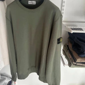 Grön tröja från Stone Island Junior - Säljer en stilren grön tröja från Stone Island Junior köpt från NK. Tröjan har en klassisk rund hals och långa ärmar. Den är dekorerad med det ikoniska Stone Island-märket på ärmen. Storlek 14 år. Passar mig som är 175 cm. Aldrig använd. Äkta som man kan se på sista bilden. Bara att höra av dig vid frågor.