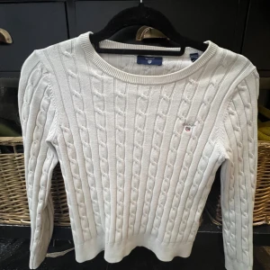 Vit stickad tröja från GANT - Säljer en stilren vit stickad tröja från GANT med klassiskt flätmönster. Tröjan har långa ärmar och rund halsringning. Passar barn i åldern 11-12 år. En tidlös och bekväm tröja för alla tillfällen. Den är lite smutsig runt halsen.