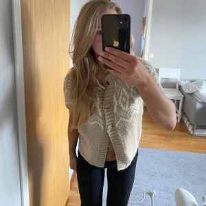 Beige stickad kofta från Only - Säljer en mysig beige stickad kofta från Only med ett vitt mönster. Koftan har korta ärmar och stora knappar framtill. Super snygg till våren! 