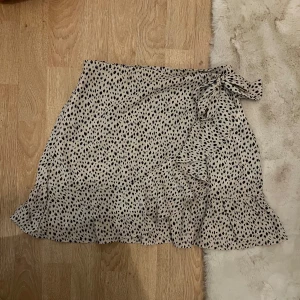 Omlottkjol - Snygg omlottkjol från shein i svart och beige. Kjolen har volang längs botten och knytning i midjan. Köpt två år sedan, använt max 5 gånger. Storlek 38 men passar som 36 också