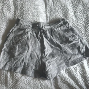 Grå shorts med snörning - Säljer ett par bekväma grå shorts med elastisk midja och snörning. Perfekta för en avslappnad dag eller träning. De är tillverkade i ett mjukt material som ger en skön känsla.