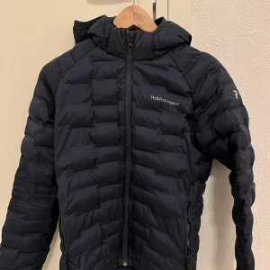 Svart dunjacka från Peak Performance - Säljer en svart dunjacka från Peak Performance. Jackan har en dragkedja framtill och är långärmad med en quiltad design. Perfekt för kyliga dagar med stilren look. 🖤