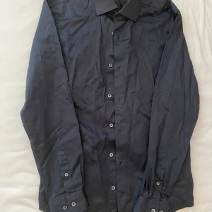 Svart skjorta från Dressmann - Snygg svart skjorta från Dressmann i premium bomull med stretch. Skjortan har en slim fit passform och långa ärmar. Perfekt för en stilren look.