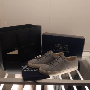 Grå sneakers från Polo Ralph Lauren - Helt oanvända snygga grå sneakers från Polo Ralph Lauren i skinn. Skorna har en stilren design med snörning och en vit sula. Perfekta för en avslappnad och trendig look. Storlek 44 men känns som 45. Pris kan diskuteras 