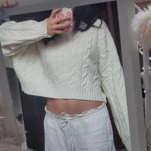 Vit stickad croppad tröja - Säljer en vit stickad tröja med kabelstickat mönster. Tröjan är croppad och har långa ärmar, perfekt för en stilren och mysig look. Passar bra till både jeans och kjol. Säljes i nyskick då den aldrig riktigt passade mig. Hör av dig vid intresse! 🤍