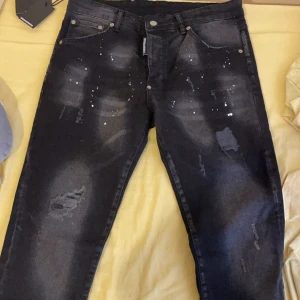Svarta jeans från Dsquared2 - Snygga svarta jeans från Dsquared2 med slitna detaljer och stänk för en cool look. De har en klassisk femficksdesign och en knappgylf. Perfekta för dig som vill ha en edgy stil. 