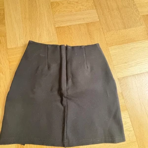 Svart kortkjol med slits - Snygg svart kortkjol med en liten slits framtill. Perfekt för en stilren look. Kjolen har en enkel design som gör den lätt att matcha med olika toppar.