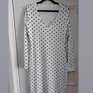 Vit prickig klänning - Snygg vit klänning med svarta prickar och v-ringning. Den har långa ärmar och en figurnära passform som framhäver silhuetten. Perfekt för en stilren look.
