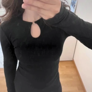 Svart ribbad tröja från BikBok - Snygg svart ribbad tröja från BikBok i storlek XS. Tröjan har en unik detalj med en ring vid halsen och långa ärmar. Perfekt för en stilren look.