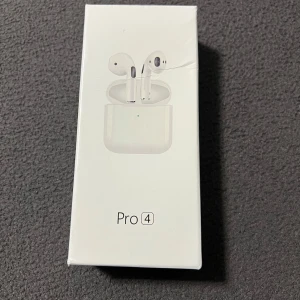 Pro 4 Trådlösa Hörlurar – Stilren Design och Modern Funktionalitet - Förpackningen visar ett par trådlösa hörlurar märkta som “Pro 4,” vilka har en design som påminner om populära true wireless-modeller på marknaden. Hörlurarna är placerade i ett kompakt laddningsfodral med en minimalistisk design, inklusive en subtil LED-indikator på framsidan. De har en smidig och ergonomisk form med inbyggda sensorer och mikrofoner för optimal ljudupptagning och användarkomfort. Förpackningen är stilren med en vit bakgrund och enkel grafik som framhäver produkten utan överflöd