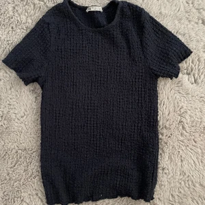 Svart ribbad topp från Zara - Säljer en svart ribbad topp från Zara i storlek S. Toppen har en texturerad yta och korta ärmar, perfekt för både vardag och fest. Den är tillverkad i Turkiet och har en bekväm passform. Passar bra till jeans eller kjol för en stilren look.