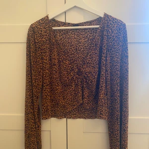 Leopardmönstrad topp från Urban Outfitters - Säljer en supercool leopardmönstrad topp från Urban Outfitters i storlek M. Toppen är croppad med långa ärmar och har en snygg knytdetalj framtill. 