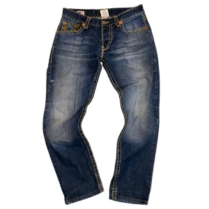 True religion jeans - Ett par svin snygga trueys med fet stitching! Fint helhetsskick men det finns några små skavanker, ett litet hål på bakre vänsterbenet och främre höger,3 små svarta sträck vid ungefär knät fram på höger ben och lite av stygnen på sidan har lossnat (har tydligare bilder på de), annars är de riktigt fina. Mått: midja tvärsöver 42cm, Ytterbenslängd 95cm. Har fler bilder på dem så det är bara att skiva för bilder eller frågor! Köp gärna via köpt nu!! (Pris går att diskuteras lite vid snabb affär)