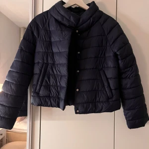 Mörkblå pufferjacka från Gina Tricot - Säljer en snygg mörkblå pufferjacka från Gina Tricot i storlek 158/164. Jackan har en stilren design med knappar framtill och är perfekt för kyliga dagar. Den är i mycket bra skick och passar perfekt för höst och vinter. Perfekt för dig som vill hålla stilen i kylan! 💙